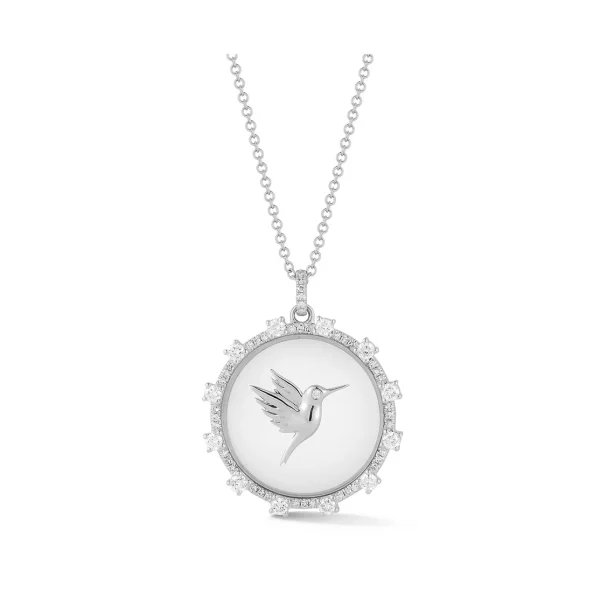 The Floating Hummingbird Necklace is a silver piece with a round pendant, engraved with a hummingbird at the center and bordered by small, sparkling stones.